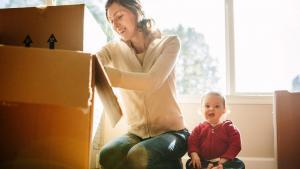 White mother and baby sitting next to stacks of boxes.